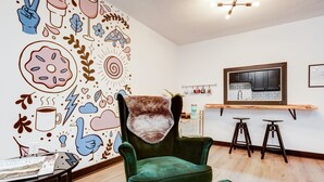 Une pièce chaleureuse avec un fauteuil en velours vert, un comptoir de bar en bois et un mur décoré d’illustrations amusantes.