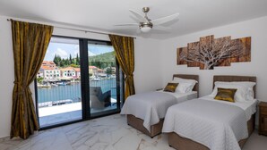 A hotel room with two beds, a ceiling fan, a large window with curtains, and a view of a marina.