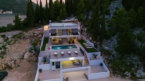 A modern multi-story house with a swimming pool, outdoor seating, and a car parked in front.
