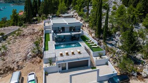 A modern two-story house with a swimming pool, surrounded by rocky terrain and pine trees.