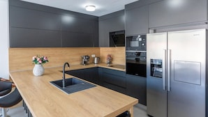 A modern kitchen with dark cabinets, a wooden countertop, a stainless steel refrigerator, and a built-in oven.