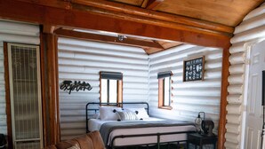 A log cabin interior with a leather sofa, a wooden table, a bed with a window, and a wall-mounted mirror. - Hiker's Haven Summary (Mount Laguna)