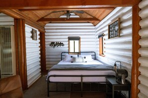 A log cabin room with a bed, a desk, a fan, and a window. - Hiker's Haven Summary (Mount Laguna)
