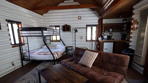A cabin interior with a bunk bed, a sofa, a coffee table, and a kitchenette. - Hiker's Haven Summary (Mount Laguna)