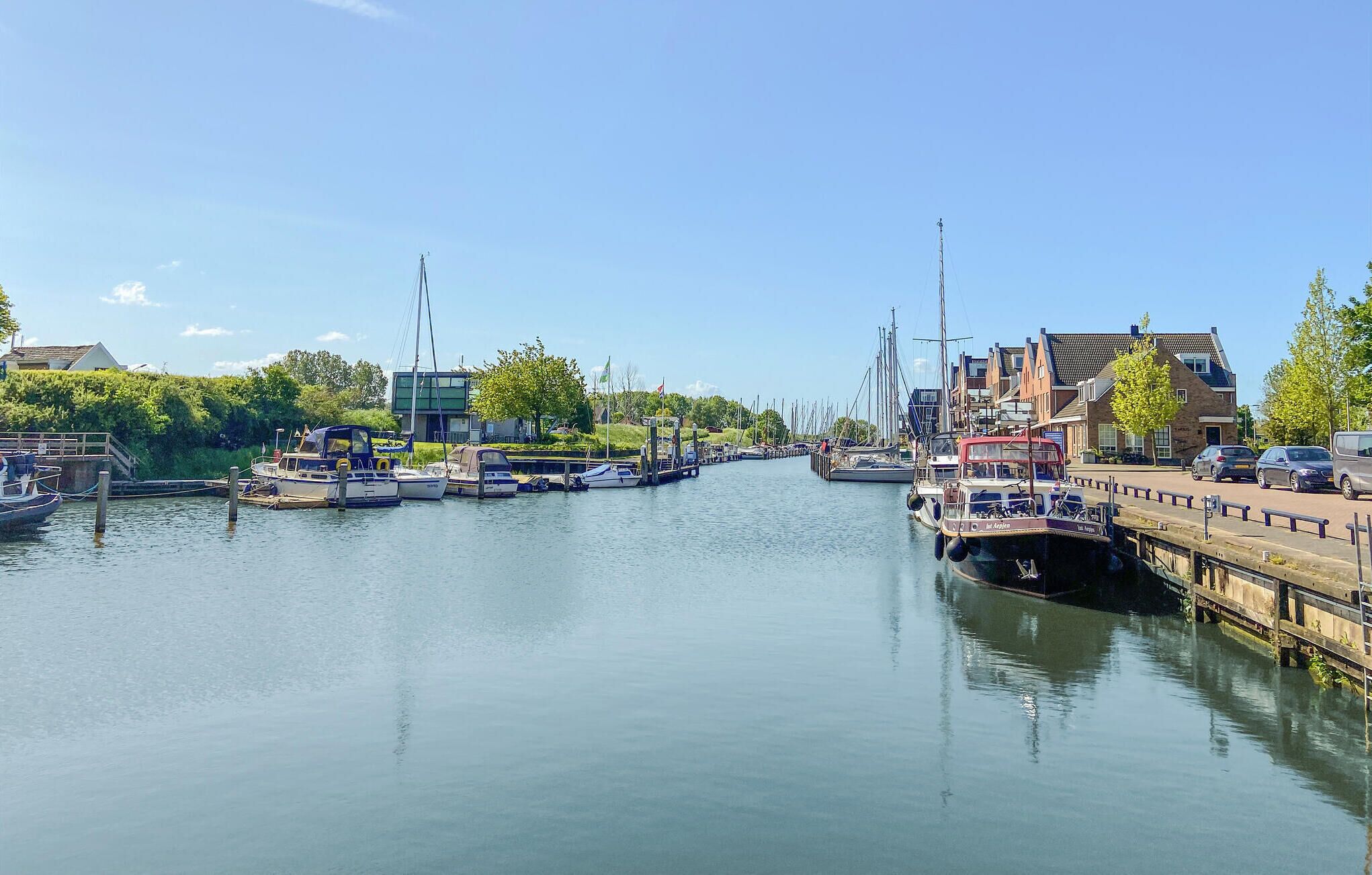 A calm waterway with boats docked on both sides, a pedestrian bridge, and buildings along the shore.