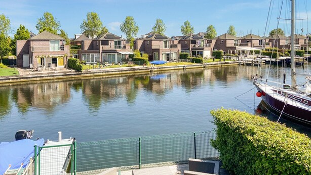 Vista de un canal con edificios residenciales, un barco amarrado a la derecha y una valla verde en primer plano.