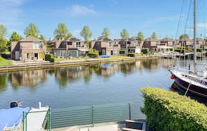Vista de un canal con edificios residenciales, un barco amarrado a la derecha y una valla verde en primer plano.