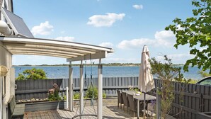 En træterrasse med pergola, udendørs møbler og udsigt til en sø.