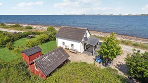 En ejendom ved kysten med et hvidt hus, et rødt skur og en lille terrasse.