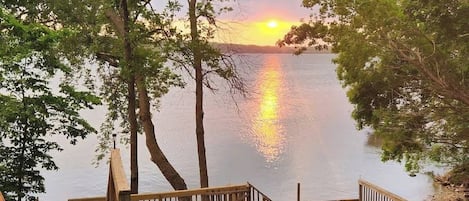A wooden deck with railings overlooking a calm lake at sunset.