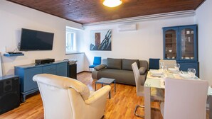 A living room with a sofa, a dining table set for two, a TV mounted on the wall, and a cabinet with glass doors. - 2 bedroom gorgeous home in Labin (Labin)