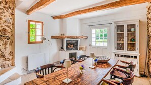 A dining room with a wooden table, chairs, a fireplace, and a cabinet with glass doors. - Awesome home in Carcès (Carcès)