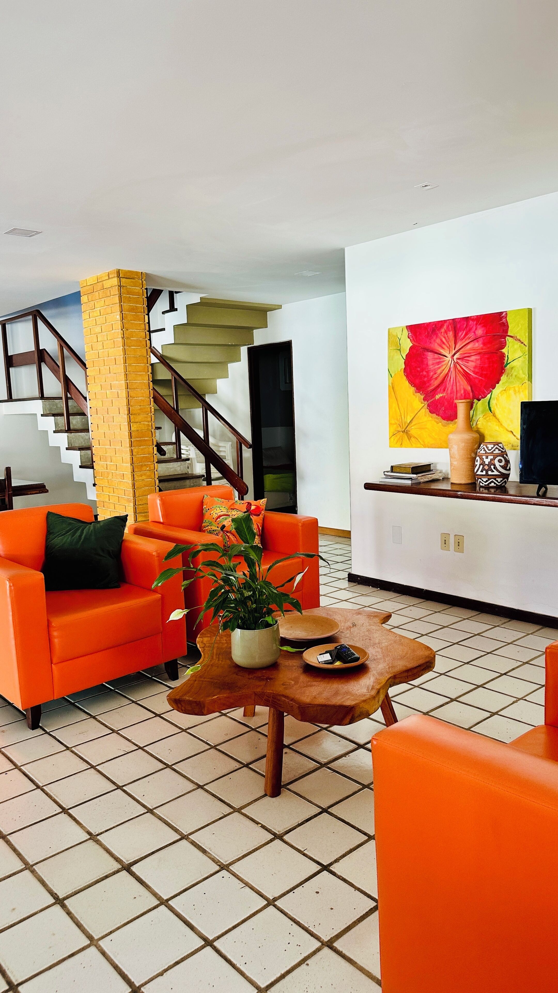 Una sala de estar moderna con muebles naranjas, una mesa de centro de madera y un cuadro grande de una flor.