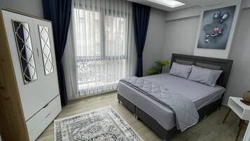 A modern bedroom with a bed, a wardrobe, a large window with curtains, and a painting on the wall.