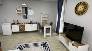 A modern living room with a flat-screen TV, a dining area with a table and chairs, a small refrigerator, and a decorative mirror with a bird decal. - Forbes Butik Otel (Izmir)