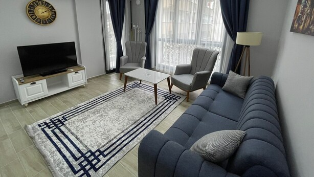 A modern living room with a sofa, armchair, TV, and a coffee table. - Forbes Butik Otel (Izmir)