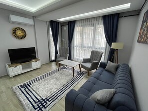 A modern living room with a sofa, armchair, TV, and a coffee table. - Forbes Butik Otel (Izmir)
