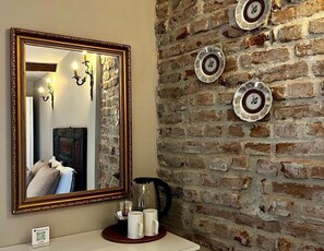 Un baño con espejo, cafetera y platos decorativos en una pared de ladrillo.