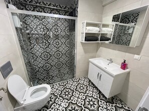 Un baño con piso estampado, un inodoro, un lavabo con espejo y una zona de ducha con cortina decorativa.