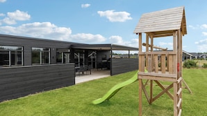 Een modern huis met een houten terras, een glijbaan en een patio.