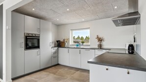 Een moderne keuken met grijze kasten, een ingebouwde oven, een raam met uitzicht en een roestvrijstalen afzuigkap.