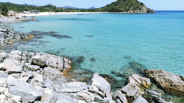 A rocky shoreline with clear turquoise water and a distant mountain. - STELLA DORADA VACANZE BEDROOMS (Castiadas)