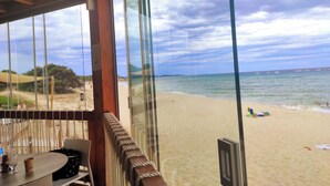 A beach view from a covered area with a table and chairs, a rope barrier, and a wooden structure. - STELLA DORADA VACANZE BEDROOMS (Castiadas)