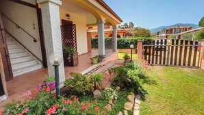 A house with a covered porch, a staircase, and a well-maintained garden with various plants and flowers. - STELLA DORADA VACANZE BEDROOMS (Castiadas)