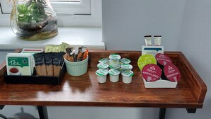 Un plateau contenant des sachets de thé, des capsules de café et des briques de lait, posé sur une table en bois près d’une fenêtre.