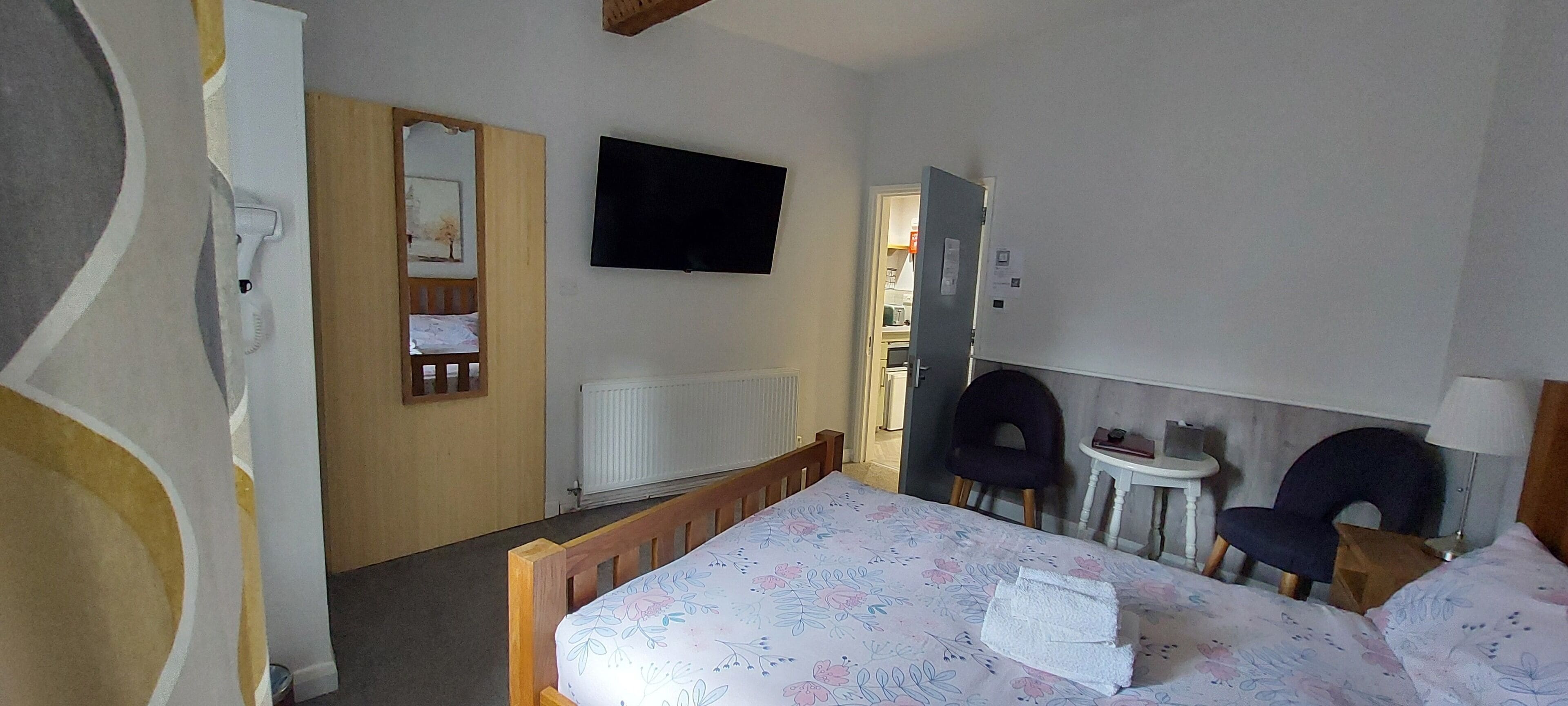 Une chambre d’hôtel avec un lit, deux chaises, une petite table, un téléviseur et un radiateur.