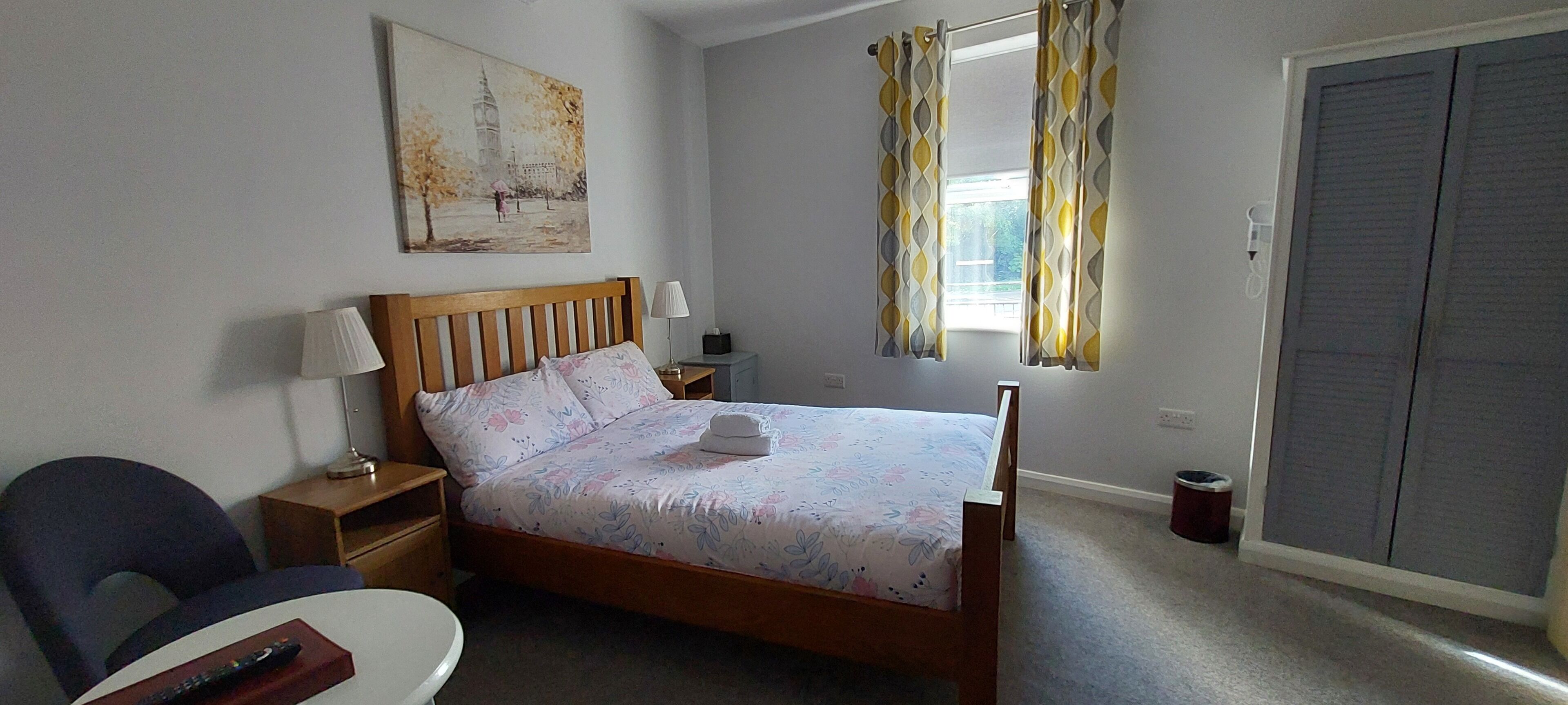 Une chambre à coucher avec un lit en bois, une table de chevet avec une lampe, une chaise et un tableau accroché au mur.