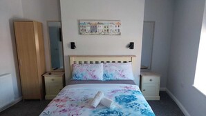 Ein Schlafzimmer mit einem Bett, zwei Nachttischen, einem Kleiderschrank, einem Spiegel und einem Wandbild.