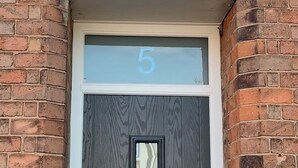 Une porte noire avec un cadre blanc, une petite fenêtre surmontée du chiffre « 5 », et une poignée en métal.