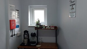 Une petite kitchenette équipée d’une machine à café, d’un pichet en verre et d’une étagère où sont posées des tasses et une plante.