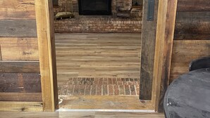 A wooden interior with a brick fireplace, a television, and a small shelf with decorative items. - Mine Lick Creek Resort 128 (Baxter)