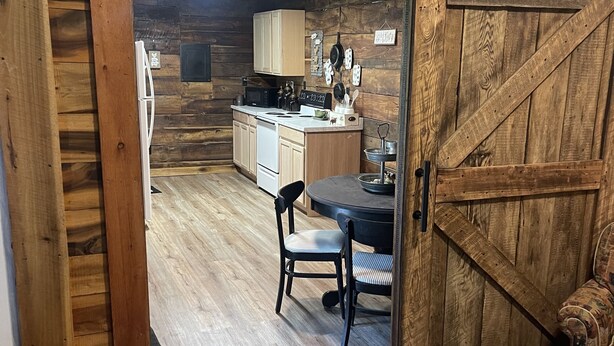 A rustic wooden interior with a kitchen area featuring wooden cabinets, a microwave, and a dining table with chairs. - Mine Lick Creek Resort 128 (Baxter)