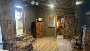 A rustic room with wooden walls and floors, a wooden cabinet, a patterned sofa, and a fireplace. - Mine Lick Creek Resort 128 (Baxter)