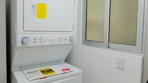 Une machine à laver blanche, avec une étiquette d’instructions jaune, un panneau de commande doté de boutons bleus et blancs, et une fenêtre en verre dépoli.