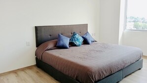 Une chambre moderne avec un grand lit, une tête de lit sombre et une fenêtre donnant sur la ville.