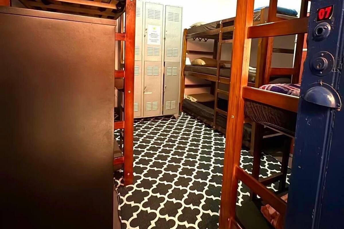 A dormitory room with bunk beds, a wardrobe, lockers, and a patterned floor.