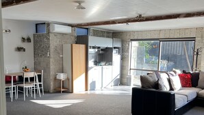 A modern living room with a black sofa, a dining area with a table and chairs, and a kitchen with white cabinets. - Cosy comfortable unit with city views (Napier)
