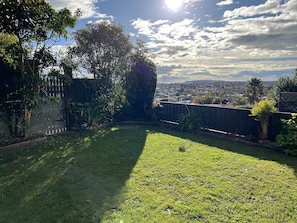 A backyard with a grassy lawn, a wooden fence, and a view of a residential area in the distance. - Cosy comfortable unit with city views (Napier)