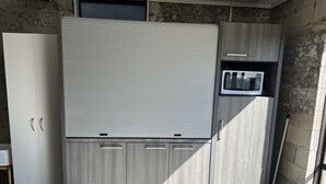 A compact kitchen with a built-in microwave, a trash bin, and a broom leaning against the wall. - Cosy comfortable unit with city views (Napier)