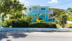 A two-story house with a balcony, surrounded by lush greenery and a white stone wall. - Complete Villa Down stairs, 2 Bedroom (Steventon)