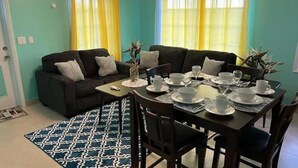 A dining area with a table set for four, a black sofa, and yellow curtains. - Complete Villa Down stairs, 2 Bedroom (Steventon)