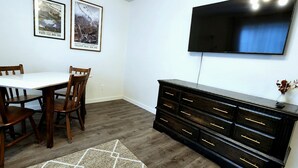 A dining area with a white table and wooden chairs, a black entertainment center with drawers, and two framed pictures on the wall. - Fireweed 2 Bedroom by airport; lakes, trails, fishing, skiing, hiking! (Anchorage)