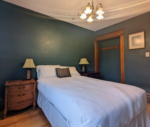 Une chambre à coucher comprenant un lit, deux tables de chevet, une commode, un lustre et un miroir.