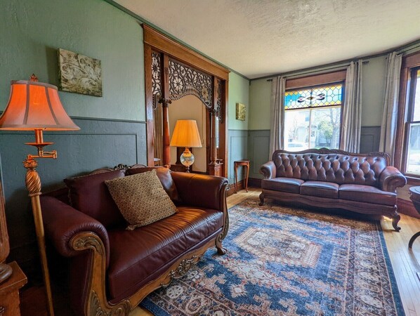 Un salon traditionnel avec un canapé en cuir marron, un tapis à motifs et une fenêtre à vitraux.