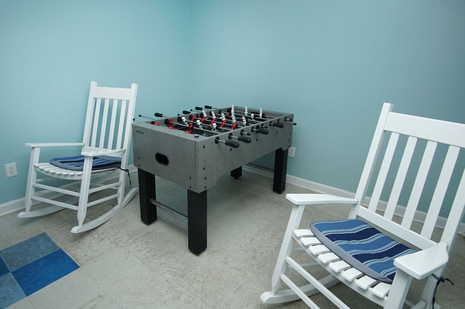 Une pièce avec une table de baby-foot, deux fauteuils à bascule et un tapis aux motifs bleus et blancs.