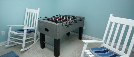 Une pièce avec une table de baby-foot, deux fauteuils à bascule et un tapis aux motifs bleus et blancs.